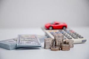 concepto de negocio de seguros de automóviles, compra de ahorro - venta con impuestos y préstamo para automóviles nuevos. vehículo de juguete de coche con dinero de moneda de pila en el fondo. planificación para administrar los costos de financiación del transporte. préstamo para coche foto