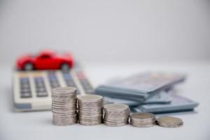 concepto de negocio de seguros de automóviles, compra de ahorro - venta con impuestos y préstamo para automóviles nuevos. vehículo de juguete de coche con dinero de moneda de pila en el fondo. planificación para administrar los costos de financiación del transporte. préstamo para coche foto