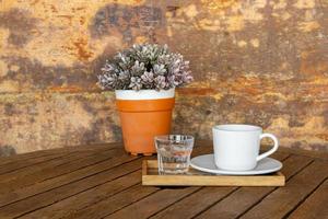 white coffee cup and glass of water on vintage wooden table and flower pot photo