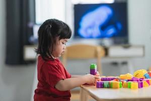 niña asiática linda y graciosa de preescolar con una camisa colorida jugando con lego o bloques de juguete de construcción construyendo una torre en la sala de jardín de infantes o en la sala de estar. niños jugando niños en la guardería. foto