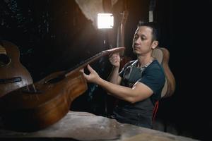 Guitar makers asian man making acoustic guitars in laboratory. Asian guitar maker builds high quality guitars for musicians handmade guitar shop. Working fine woodusic, tradition, ancient crafts. photo