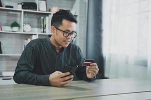 Man holding credit card and using mobile to shopping online. asian man working at home. Online shopping, e-commerce, internet banking, spending money, working from home concept. photo