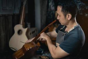 Guitar makers asian man making acoustic guitars in laboratory. Asian guitar maker builds high quality guitars for musicians handmade guitar shop. Working fine woodusic, tradition, ancient crafts. photo