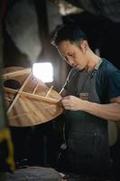 Guitar makers asian man making acoustic guitars in laboratory. Asian guitar maker builds high quality guitars for musicians handmade guitar shop. Working fine woodusic, tradition, ancient crafts. photo