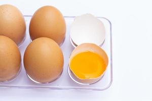 Four brown eggs lay on an egg tray with an eggshell on a white background. There was a broken egg, showing the yolk inside. photo