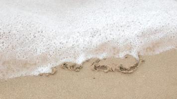 2022 escribe a mano cifras en la playa de arena para feliz año nuevo 2023, la ola del mar se lleva el número escrito a mano en el mar de arena de la playa dorada. adiós 2022