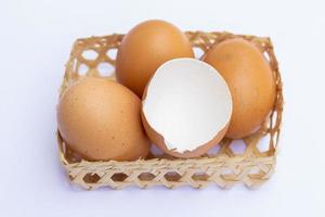 los huevos de gallina marrones se colocan en bandejas de bambú. con una cáscara de huevo sobre un fondo blanco foto