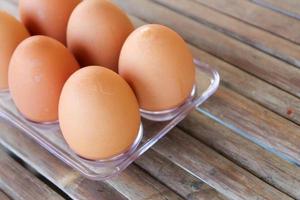 close up Six brown eggs in plastic box on bamboo table with one broken boiled egg, top view. photo