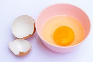 yema de huevo en un tazón rosa con una cáscara de huevo en el fondo blanco foto