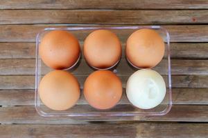 close up Six brown eggs in plastic box on bamboo table with one broken boiled egg, top view. photo