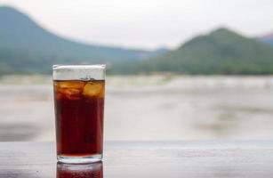 Cola in glass on table with mountain and river background photo