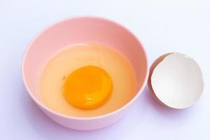 yema de huevo en un tazón rosa con una cáscara de huevo en el fondo blanco foto