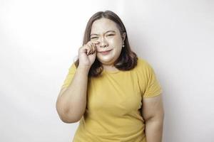A portrait of an Asian big sized woman wearing a yellow t-shirt isolated by white background looks depressed photo