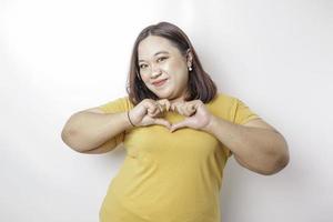 An attractive young Asian big size woman wearing a yellow t-shirt feels happy and a romantic shapes heart gesture expresses tender feelings photo