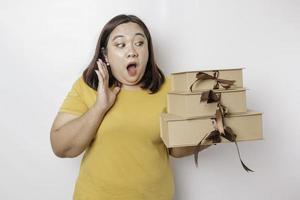 A shocked young Asian big sized woman is wearing yellow shirt and holding presents boxes and shopping bags. photo