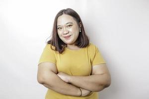 retrato de una mujer asiática de gran tamaño, sonriente y confiada, con camisa amarilla, de pie con los brazos cruzados y mirando la cámara aislada sobre fondo blanco foto