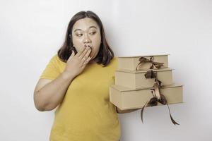 A shocked young Asian big sized woman is wearing yellow shirt and holding presents boxes and shopping bags. photo