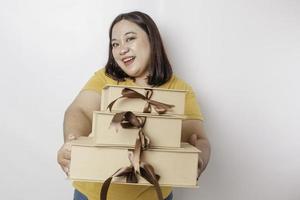 A happy young Asian big sized woman is wearing yellow shirt and holding presents box and shopping bag. photo