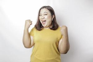 una joven mujer asiática de gran tamaño con una expresión feliz y exitosa que lleva una camisa amarilla aislada por un fondo blanco foto