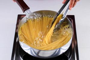 Women Cooking Spaghetti in Pan of Boiling Water in the Kitchen photo