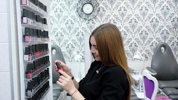 Smiling happy pretty woman chooses from wide range of nail polish in beauty saloon before procedure video
