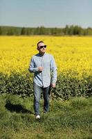 A young man in sunglasses is walking and having fun through a Sunny yellow rapeseed field, the concept of travel and freedom. summer holiday background photo