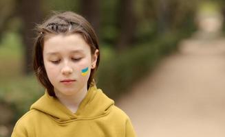 the face of a frightened girl, painted on her cheek in the yellow-blue colors of the Ukrainian flag, a request for help. Children ask for peace. High quality photo. High quality photo