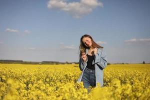 joven mujer hermosa en un campo con colza floreciente amarilla. chica en campo floral amarillo, plantación de colza, concepto de vacaciones de verano foto