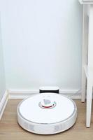 Robotic vacuum cleaner on laminate wood floor charging from base station. Smart cleaning technology. robot vacuum cleaner return to charging at dock in clean room floor photo