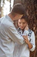 Young couple in love hugging near trees in summer park. pretty woman and man, wearing in denim outfit are having fun and have date outdoors. Romantic relationship. valentines day photo