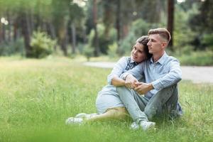 Outdoor shot of young happy couple in love sitting on grass on nature. Man and woman hugging, sunlight in summer park. Happy family in the evening sun light. The concept holiday