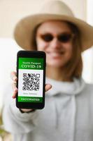 A defocused young girl is holding a passport and a smart phone with a certificate of vaccination against the Covid-19 disease. focus on the smart phone. Health Passport concept photo