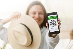 A defocused young girl is holding a passport and a smart phone with a certificate of vaccination against the Covid-19 disease. focus on the smart phone. Health Passport concept photo