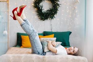 Portrait of gorgeous brunette woman in red high heels is having fun in bed and posing in the Christmas decorated interior. photo