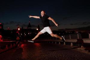 Adult young man in black t shirt and white shorts is jumping and having fun near the old castle in the evening. Fun concept, Kamyanets Podilskyy, Ukraine photo