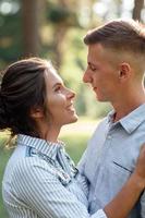 Cheerful young woman and man are hugging outdoors in summer park. Dating and romantic vacation. couple in love gently looking at each other on sunny day. Love and relationships between young people photo