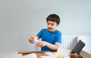 Happy school boy learn how to making origami Swan paper. Kid learning paper art origami lesson, Child having fun doing Art and Craft at home, Home schooling,Back to school concept photo