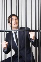 I am not guilty Terrified young man in formalwear standing behind a prison cell and looking up photo