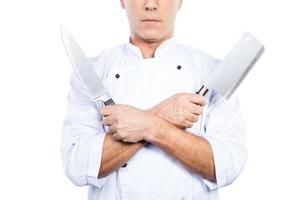 Chef with knifes. Close-up of confident mature chef in white uniform holding knifes in his hands while standing against white background photo