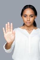 Stop Attractive young African woman showing her palm while keeping her hand outstretched and standing against grey background photo