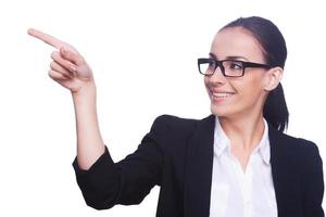 Look at that Cheerful young woman in formalwear and eyeglasses pointing away and smiling while standing isolated on white photo