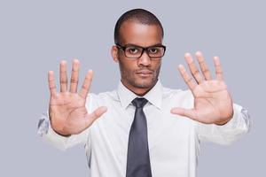 Stop Young African man in shirt and tie showing his palms and looking at camera while standing against grey background photo