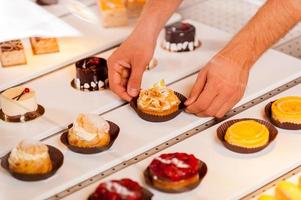 Is this your choice Close-up of male hand taking a cupcake from showcase while standing in bakery shop photo