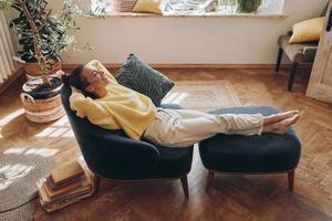 vista superior de una mujer feliz manteniendo los ojos cerrados mientras se relaja en una silla cómoda en casa foto