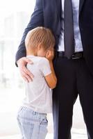 I will be missing you Little boy crying and covering face with hands while his father in formalwear consoling him photo