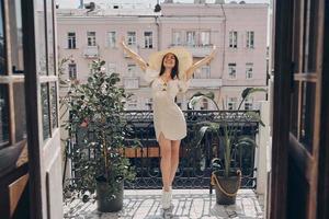 Full length of excited young woman in elegant hat keeping arms outstretched while relaxing on the balcony photo