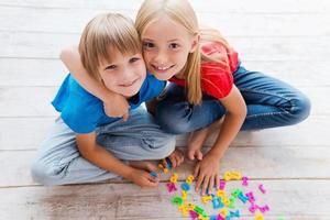 We are good friends Top view of two cute little children looking at camera and smiling while sitting on the floor and playing with plastic colorful letters photo