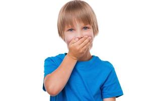 Oops Frustrated little boy covering mouth with hand and looking at camera while standing isolated on white photo