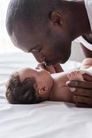 You are my little angel Side view of happy young African man playing with his little baby and smiling while lying in bed photo