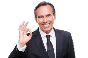 Everything is OK Happy mature man in formalwear looking at camera and smiling while gesturing OK sign and standing against white background photo